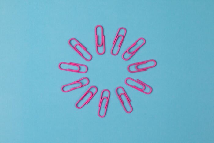 10 pink-colored paperclips are arranged in a circle in front of a bright blue background